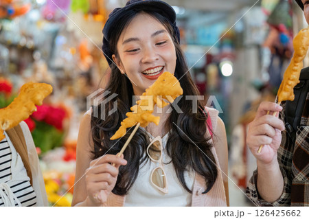 Friends sharing excitement over street food, enjoying crispy treats while traveling through a colorful market 126425662