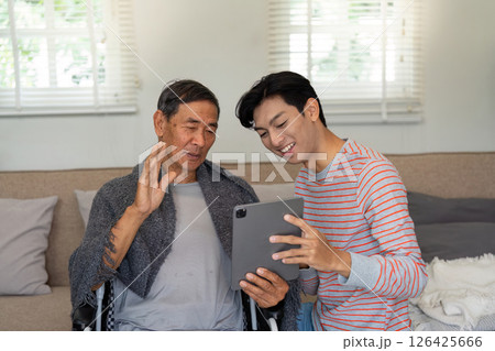 Elderly man in wheelchair waving at son while video chatting on tablet. 126425666