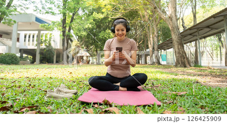 Wellness and Routine. A woman sitting cross-legged outdoors, engaging with her phone as part of her wellness practice. 126425909