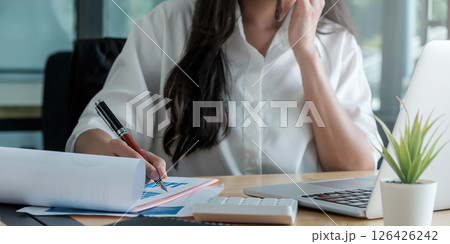 Close up of businesswoman or accountant hand holding pen working on laptop computer for calculate business data, accountancy document and calculator at office, business concept Close up of businesswoman or accountant hand holding pen working on laptop computer for calculate business data, accountancy document and calculator at office, business concept 126426242