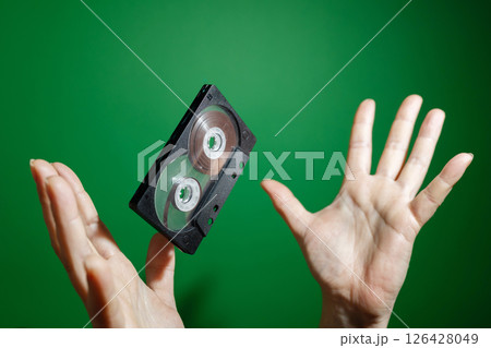 A Flying VHS Tape is Held in Hands Against a Vibrant Green Background in Artistic Style 126428049