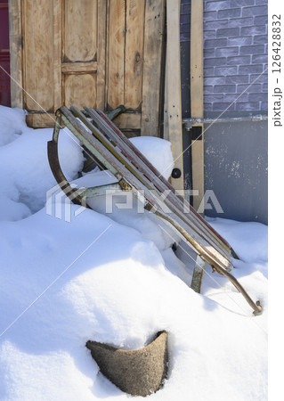 An old children's sled in a snowdrift near wooden doors 126428832