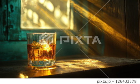 Glass of whisky with ice glows warmly on wooden table as sunlight streams through window creating peaceful world day scene 126432579