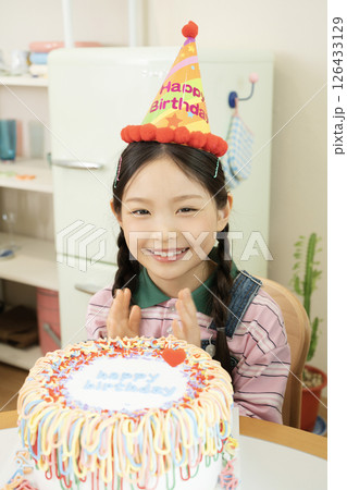 Cute little girl wearing a cone hat and sitting in front of a cake 126433129