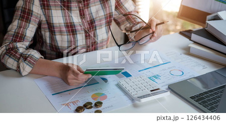 Young Asian woman checking bills, taxes, bank account balance and calculating credit card expenses. Family expenses concept. Young Asian woman checking bills, taxes, bank account balance and calculating credit card expenses. Family expenses concept. 126434406