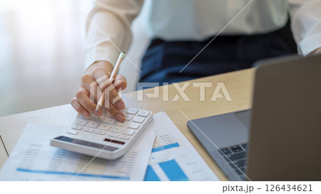woman calculating individual income tax from financial document during note some data to sticky on window glass with calculator. woman calculating individual income tax from financial document during note some data to sticky on window glass with calculator. 126434621