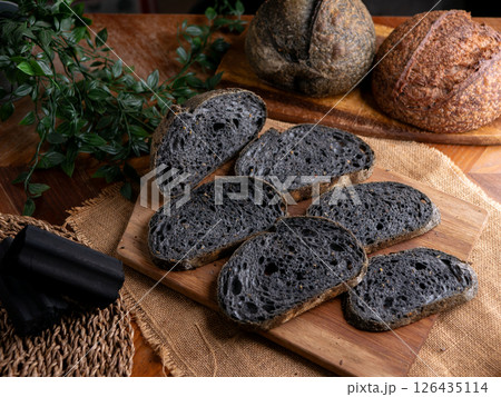 Fresh baked black charcoal sourdough ciabatta bread sliced on wooden board. 126435114