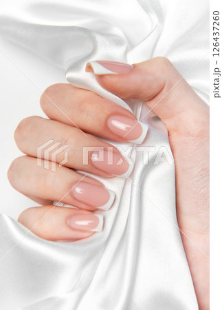 Woman hand showing french manicure on white silk background Woman hand showing french manicure on white silk background 126437260