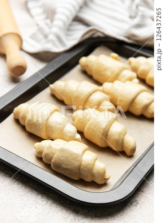 Raw croissants baking on tray with rolling pin and kitchen towel 126437265