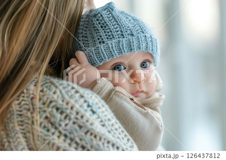 Loving mother hugs little baby at home. Pretty woman holding cuddling newborn child in her arms. Happy family together. Young mom carrying kissing small infant on hands. Knitted warm winter clothes 126437812
