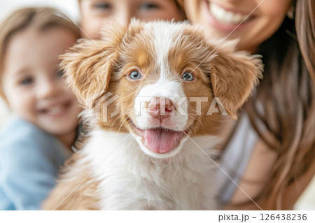 Happy moment with a fluffy brown and white puppy in focus, surrounded by a smiling family in the background. 126438236