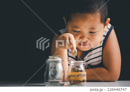 Young boy learns to save money by studying finance, collecting coins, and understanding the importance of investment and saving for children. boy, save, money, study, children, person, coin, finance. 126440747