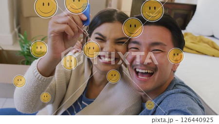 Image of smiley face icons over happy biracial couple with house key Image of smiley face icons over happy biracial couple with house key 126440925