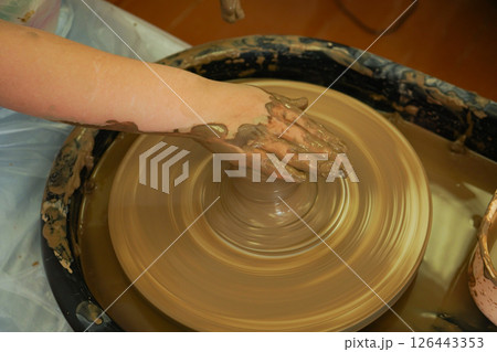 The potter's wheel. A close-up of the hands of a craftsman skillfully working with clay on a potter's wheel, giving it the shape of a clay product The potter's wheel. A close-up of the hands of a craftsman skillfully working with clay on a potter's wheel, giving it the shape of a clay product 126443353
