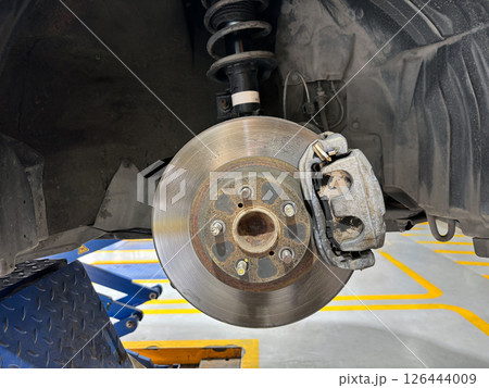 A car's brake assembly is under inspection at an auto repair facility. The technician assesses the brake disc, caliper, and suspension component for any need repair. 126444009