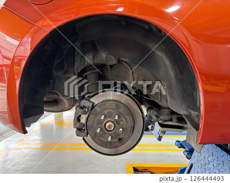 A car's brake assembly is under inspection at an auto repair facility. The technician assesses the brake disc, caliper, and suspension component for any need repair. A car's brake assembly is under inspection at an auto repair facility. The technician assesses the brake disc, caliper, and suspension component for any need repair. 126444493