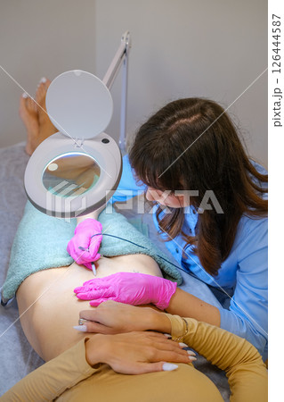 Young beautiful female dermatologist doing hair removal treatment on patient's bikini zone with electrolysis. Epilation and beauty concept. High quality photo 126444587