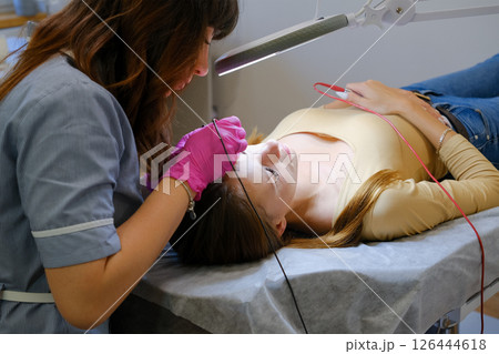 Young beautiful female dermatologist doing hair removal treatment on patient's face with electrolysis. Epilation and beauty concept. High quality photo 126444618