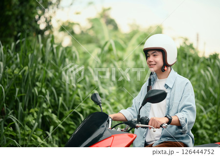Smiling young man wearing helmet riding a red motorcycle on a quiet residential street Smiling young man wearing helmet riding a red motorcycle on a quiet residential street 126444752
