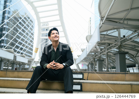 Confident businessman sitting on steps in urban cityscape and looking up with optimism 126444769