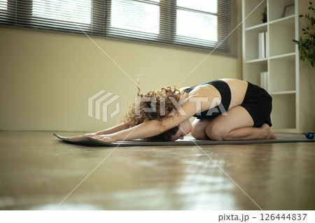Young woman doing yoga asana child's pose on mat for flexibility and relaxation 126444837