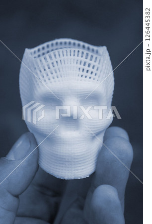 Person holding in fingers of hand small white prototype of human skull 3D printed from molten plastic on black background. Three-dimensional model. Additive technology. Printing industry. Blue color 126445382
