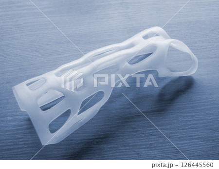 Hand splint corset prosthesis printed on 3D printer from molten white plastic powder on table. Medical orthosis fixator plastic overlay created on 3D printer. New modern medical 3D printing technology Hand splint corset prosthesis printed on 3D printer from molten white plastic powder on table. Medical orthosis fixator plastic overlay created on 3D printer. New modern medical 3D printing technology 126445560