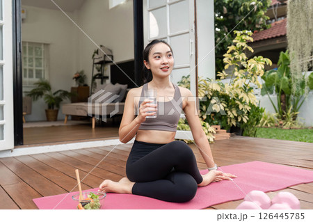 Yoga and Hydration. Young woman practicing yoga while enjoying a refreshing drink at home. 126445785