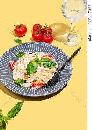 Creamy spaghetti with cherry tomatoes, cheese and basil on a plate on a yellow background 126447368