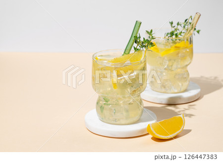 Two glasses of fresh drink lemonade with lemon, thyme and ice on a yellow background with shadows. Two glasses of fresh drink lemonade with lemon, thyme and ice on a yellow background with shadows. 126447383