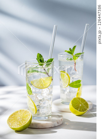 Two glasses mojito cocktail with lime, mint, ice and tube on a white blue background with shadows. Two glasses mojito cocktail with lime, mint, ice and tube on a white blue background with shadows. 126447386