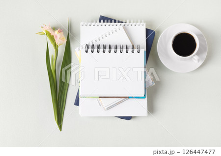 Composition with opened blank notepad, cup of black coffee, gladiolus flowers on a gray background. Festive office desktop concept. Morning coffee cup. 126447477