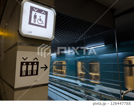 Modern metro station with moving train in the background and clear elevator signs for passengers including people with disabilities, promoting accessibility and public transport infrastructure Modern metro station with moving train in the background and clear elevator signs for passengers including people with disabilities, promoting accessibility and public transport infrastructure 126447788