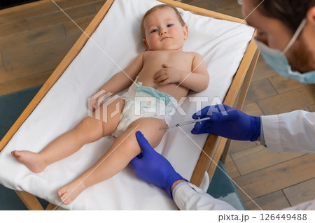 Cute baby boy lying on a table while doctor making vaccination to him 126449488