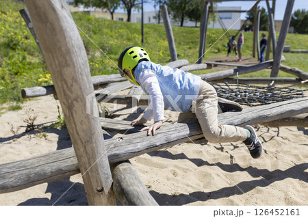 Child crawling on wooden beam at playground wearing helmet 126452161