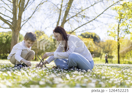 Mother and son building a small teepee with branches in a field of daisies 126452225