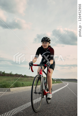 Cyclist leaning forward on bike with strong grip, motion frozen in active moment, stormy clouds and guardrail curve ahead. 126452908