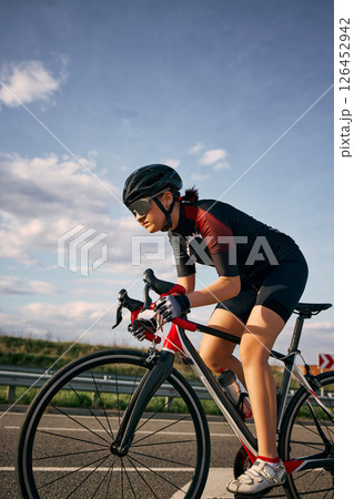 Dynamic side view photo of cyclist in aerodynamic posture gripping handlebars, highlighting bike frame, riding to finish. 126452942