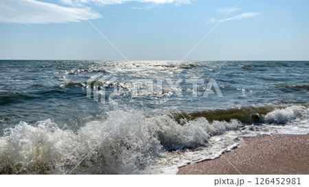 Dynamic close-up view of ocean waves crashing onto the sandy beach under a bright sun 126452981