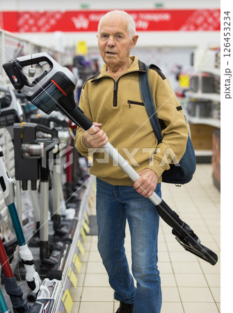 Senor man pensioner buying Upright Vacuum Cleaner in showroom of electrical appliance store Senor man pensioner buying Upright Vacuum Cleaner in showroom of electrical appliance store 126453234