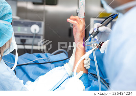 Group of orthopedic surgeons performing a wrist arthroscopy on a male patient. Female doctor performing a surgery. Orthopedic surgeon. Surgery and insurance concept. Group of orthopedic surgeons performing a wrist arthroscopy on a male patient. Female doctor performing a surgery. Orthopedic surgeon. Surgery and insurance concept. 126454224