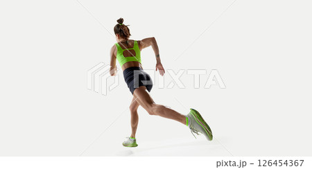 Back view of sportive woman sprinting forward during training session in studio with bright light. 126454367