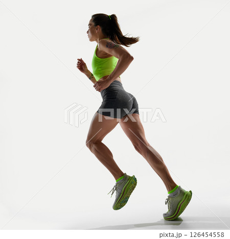 Female athlete sprinting with power and focus over white studio background, showing muscles and dynamic movement. Female athlete sprinting with power and focus over white studio background, showing muscles and dynamic movement. 126454558