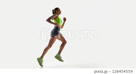 Energetic woman athlete in running pose, training, wearing bright green top and gray shorts on white background 126454559
