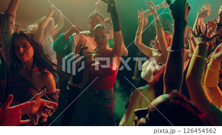 Crowd dancing energetically at a vibrant party with colorful lighting. 126454562