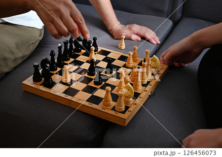 A grandmother and a teenage granddaughter are enthusiastically playing chess on a cozy sofa, demonstrating strategy and concentration in a cozy living room environment 126456073