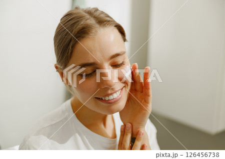 A Smiling Woman is Happily Enjoying Her Skincare Routine While at Home, Feeling Radiant A Smiling Woman is Happily Enjoying Her Skincare Routine While at Home, Feeling Radiant 126456738