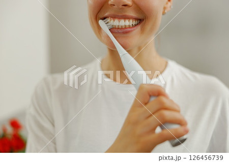 A Bright Smile A Woman Brushing Her Teeth with an Electric Toothbrush in the Bathroom 126456739