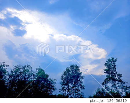 Bright afternoon sky with fluffy clouds over green trees swaying in the breeze Bright afternoon sky with fluffy clouds over green trees swaying in the breeze 126456810