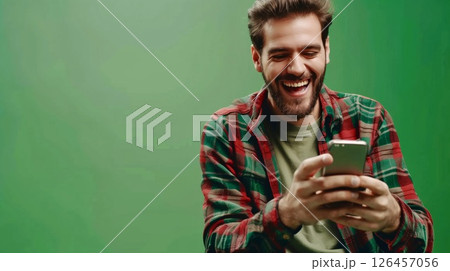 Happy man smiling at smartphone while sitting in front of green background during the day 126457056